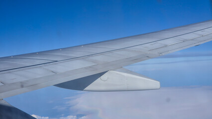 Airplane wing against a clear blue sky, captured from a window during flight. This view evokes...