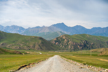 A long dirt road extending through a wide, green mountain valley towards a range of rugged peaks...