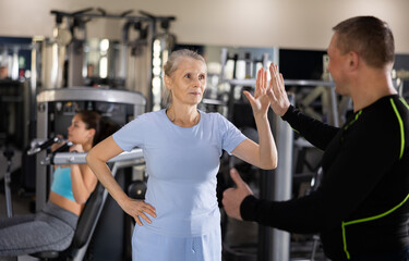 Pleased mature woman thanking her male trainer at the gym