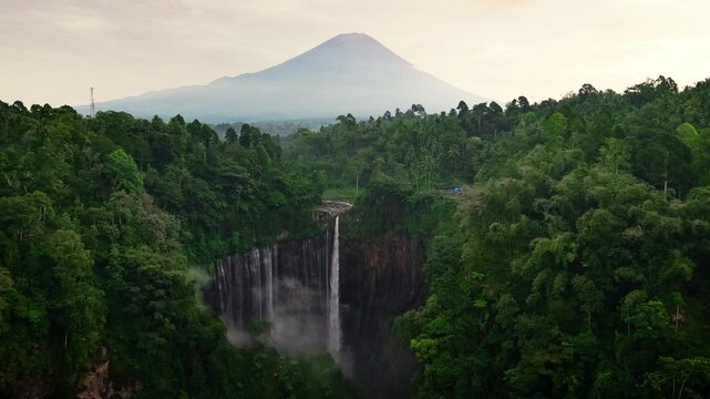 Aerial drone video flying over to the beautiful Tumpak Sewu Waterfall in East Java, Indonesia, The waterfall cascades down steep cliffs into a lush green canyon, surrounded by tropical forest.