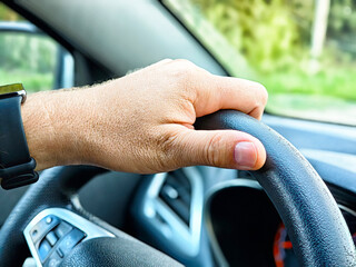Hand gripping steering wheel while driving on a sunny day in a rural area