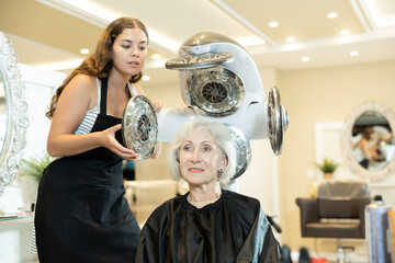 Cheerful friendly young female hairdresser adjusting settings of modern thermostimulator for drying...