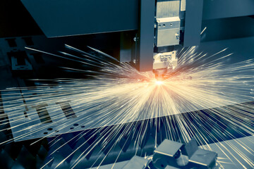 CNC laser cutting metal sheet with bright sparkle in factory.