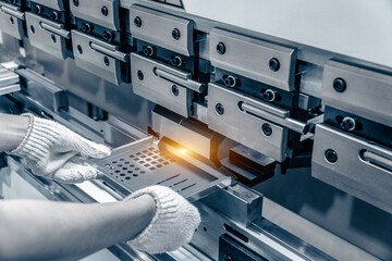 The technician operator working with sheet metal on CNC hydraulic press brake. He puts the part and bends it into a large machine at an angle.