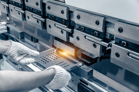 The technician operator working with sheet metal on CNC hydraulic press brake. He puts the part and bends it into a large machine at an angle.