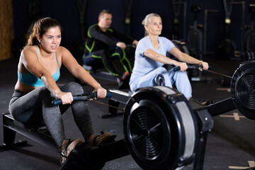 Portrait of concentrated young girl doing intense full body workout in gym, exercising on rowing...