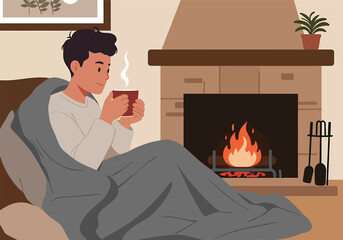 A young man enjoys a warm beverage while wrapped in a blanket by a cozy fireplace.
