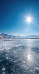 Fototapeta premium Frozen lake under a bright blue sky, snowy mountains in the background