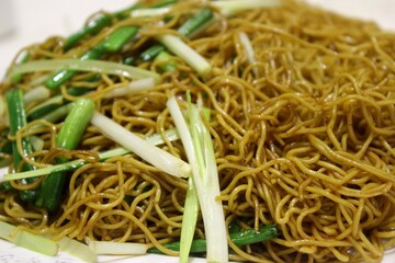 Golden stir-fried soy sauce egg noodles with Chinese green onions on white plate