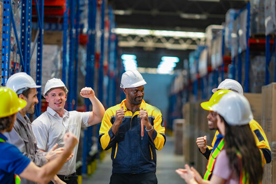 Diverse team celebrates a male coworker's success in a logistics facility. Great image for inclusion, recognition, and achievement stories.