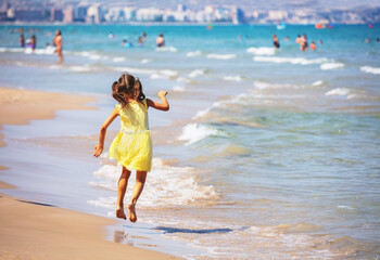 Activity on the beach in summer. Happy little girl runs on the beach. The kid in the yellow dress