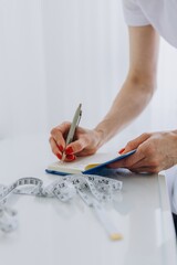 Nutritionist or cosmetologist writes down body measurements after evaluation. Tape measure on...