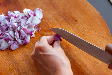 Indonesian woman hand slicing shallots on solid wooden cutting board, shot with shallow depth of field