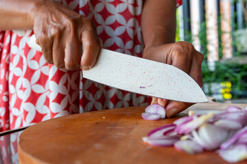 Indonesian woman hand slicing shallots on solid wooden cutting board, shot with shallow depth of...