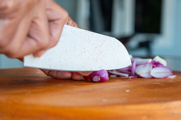Indonesian woman hand slicing shallots on solid wooden cutting board, shot with shallow depth of field