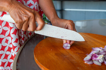 Indonesian woman hand slicing shallots on solid wooden cutting board, shot with shallow depth of field