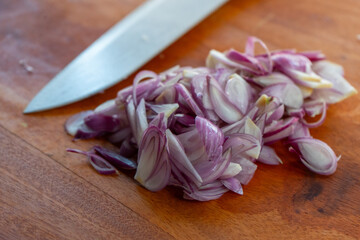 Pile of sliced shallot on a solid wooden cutting board, shot with shallow depth of field