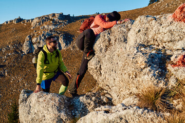 A fit and adventurous couple helps each other climb to the mountain summit during a breathtaking...