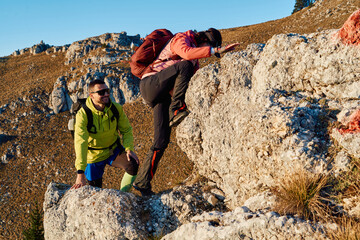 A fit and adventurous couple helps each other climb to the mountain summit during a breathtaking...