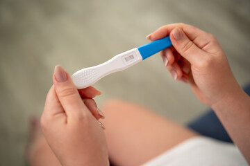 Close-up of female hands holding a pregnancy test with a positive result.