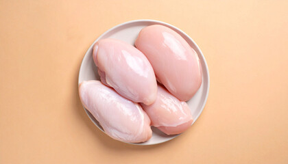 A top-down view of four raw chicken breasts on a white plate against a light orange background.
