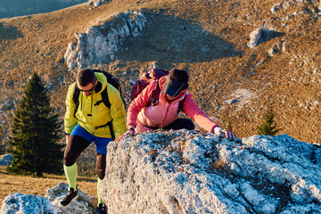 A fit and adventurous couple helps each other climb to the mountain summit during a breathtaking...