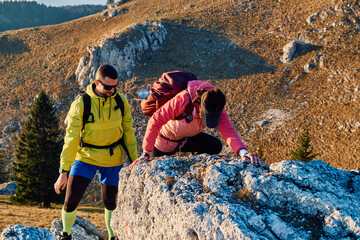 A fit and adventurous couple helps each other climb to the mountain summit during a breathtaking...