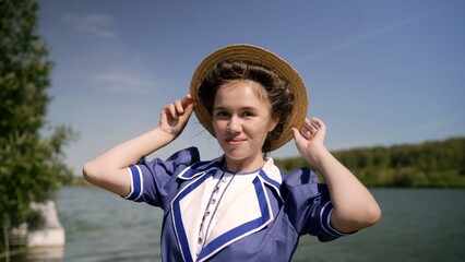 Elegant woman adjusting straw hat by the lake