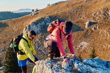 A fit and adventurous couple helps each other climb to the mountain summit during a breathtaking...