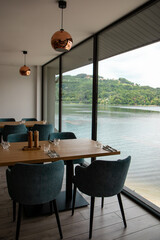 A close-up view of a set table in a modern restaurant, offering a stunning side-angle perspective of a serene lake and forested hills through large panoramic windows