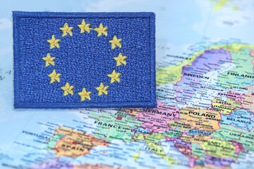 Naklejka premium Embroidered European Union flag made from thread and cloth, positioned over Europe on a world map. Represents global diplomacy, eco travel and EU identity.