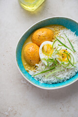 Turquoise bowl with basmati rice and curried eggs on a light-beige stone background, high angle view, vertical shot
