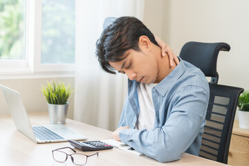 Body muscles stiff problem, ache asian young man pain neck and shoulder while sitting work on chair at home, male holding massaging rubbing, hurt or sore body. Healthcare people, office syndrome.