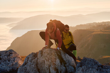A fit and adventurous couple helps each other climb to the mountain summit during a breathtaking...