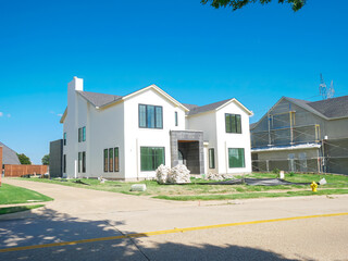 Close-up new residential build and under-construction grey home with metal scaffolding, wooden fencing, back-alley, progress in suburban architecture, sparse tree coverage and open skies, Dallas