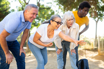 Fototapeta premium Happy casual, diverse pensioners exercising together petanque in fresh air in a sunny park in Spain