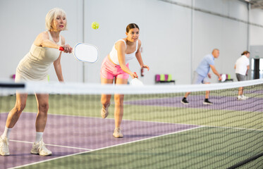 Athletic womens playing pickleball tennis on the pickleball court indoors