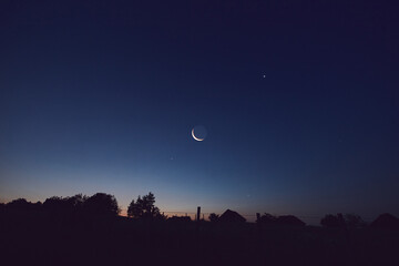 Morning old Moon with stars, planets and rural countryside tree silhouettes.