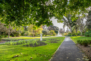 Obraz premium Peaceful garden path in Geelong Botanic Gardens, Australia. Featuring manicured lawns, ornamental flower beds, and classical statues and lush greenery. A local attraction in regional Victoria