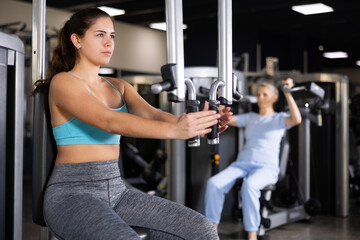 Focused sportswoman working out arm muscles on the simulator in the gym