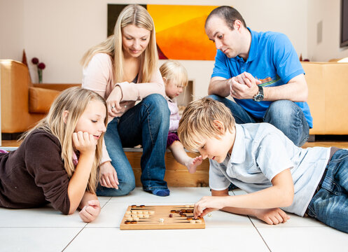 Family Life, Backgammon. A domestic scene with a young family spending time together playing a board game in the living room. From a series of related images.