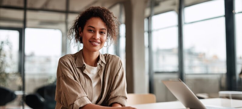 The confident woman smiling in a bright modern office environment with a laptop.