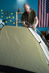 Bearded man preparing for a hike, laying out and assembling a tent at home