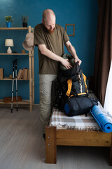 Bearded man packing backpack on bed preparing for hike at home. Travel, hiking and tourism