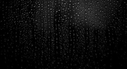 Obraz premium Monochrome Raindrops: A close-up shot showcases a delicate dance of raindrops cascading downwards against a dark surface, forming a mesmerizing play of texture, shadow, and water droplets.