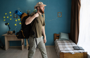 Portrait of bearded hiker with backpack getting ready for a hike standing in a room at home