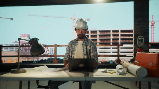 Construction site engineer working on laptop with blueprints