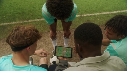 African American youth soccer coach showing tactical field diagram on tablet to teen players during outdoor practice, as they discussing strategy and preparing for their next move on field - Powered by Adobe