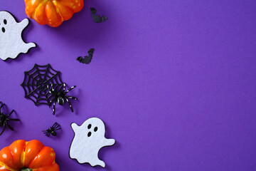 Flat lay Halloween decorations with pumpkins, ghosts, bats, spiders, and webs on vibrant purple...