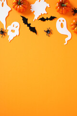 Festive Halloween flat lay with pumpkins, paper ghosts, bats, and spiders on orange background. Top...